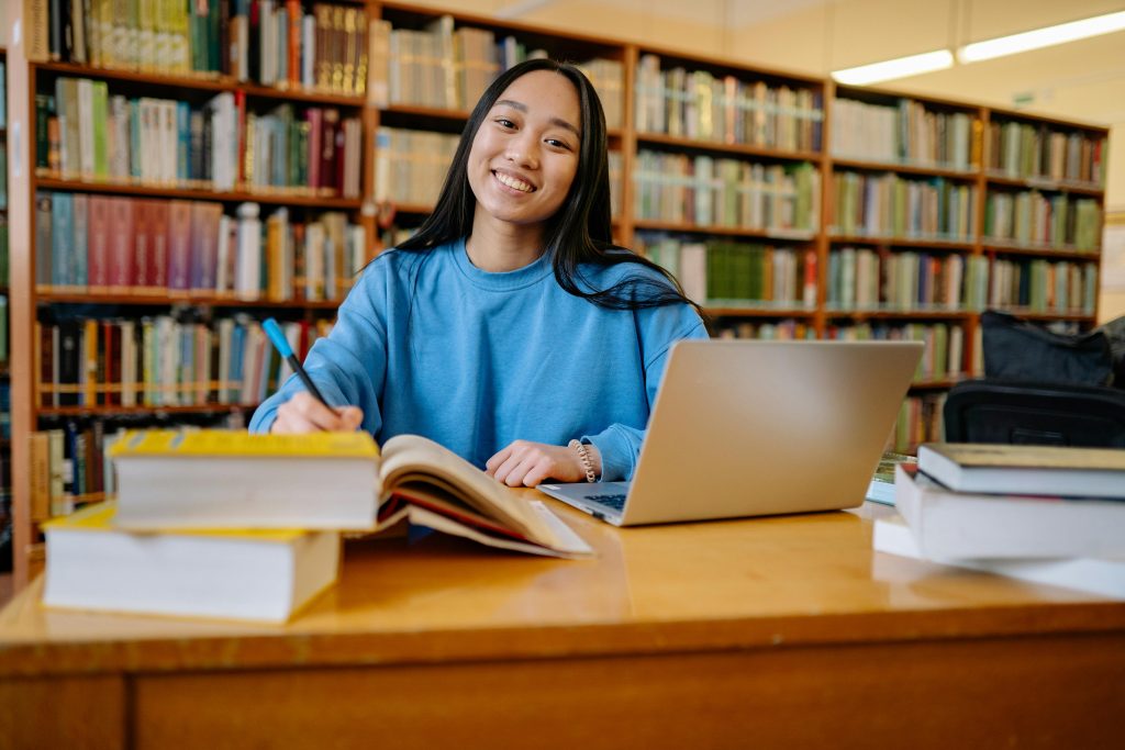 How Indian Students Choose the Right Country for Higher Studies 3 Smiling student studying in a library with books and laptop, showcasing education and focus.